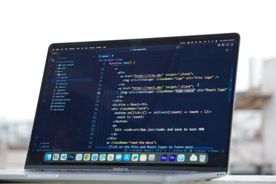 A close-up view of a MacBook Pro laptop displaying a dark-themed code editor window with lines of programming code written in HTML, CSS, and JavaScript. The screen shows sections of code with colourfu